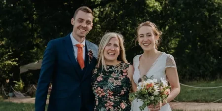 Photo of Sam White Celebrant standing in between a groom and bride after a woodland ceremony.